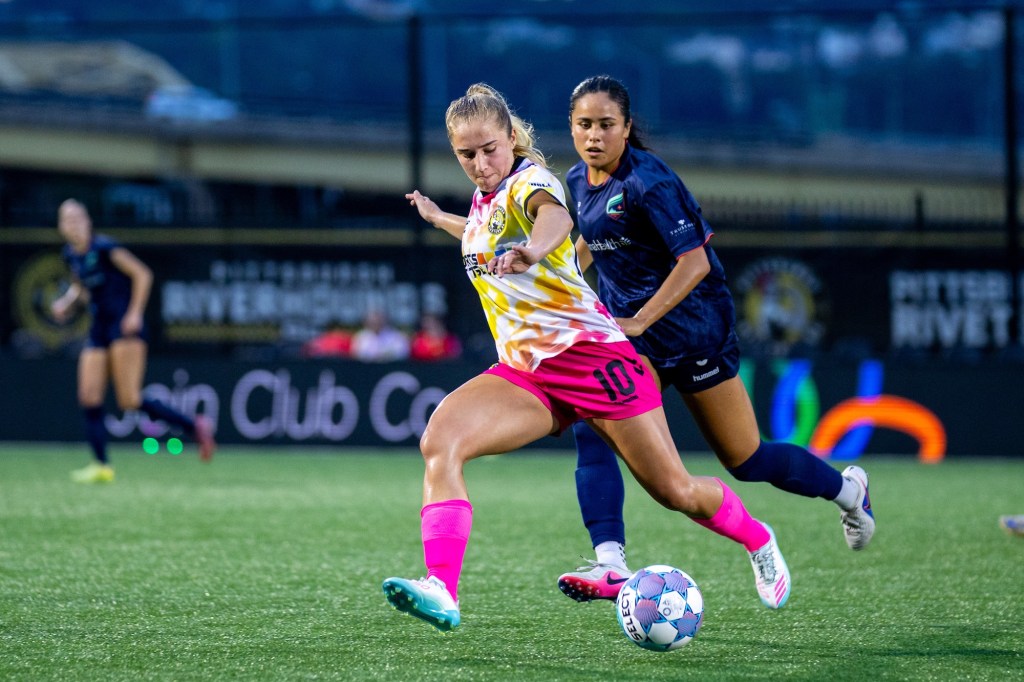 Ellen Molloy strikes a pass with a defender trailing her in the Pittsburgh Riveters playoff match against Minnesota Aurora FC on July 5, 2026 at F.N.B. Stadium in Pittsburgh. (Photo: Chris Cowger/Riveters SC)